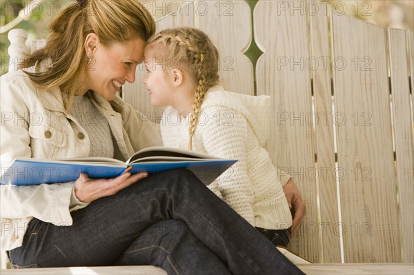 Mother reading to daughter on porch swing. Date : 2008