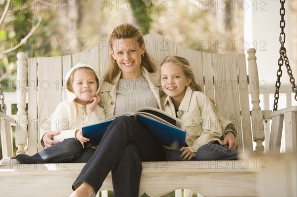 Mother reading to daughters on porch swing. Date : 2008