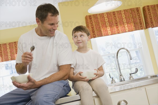 Father and son eating breakfast on kitchen counter. Date : 2008