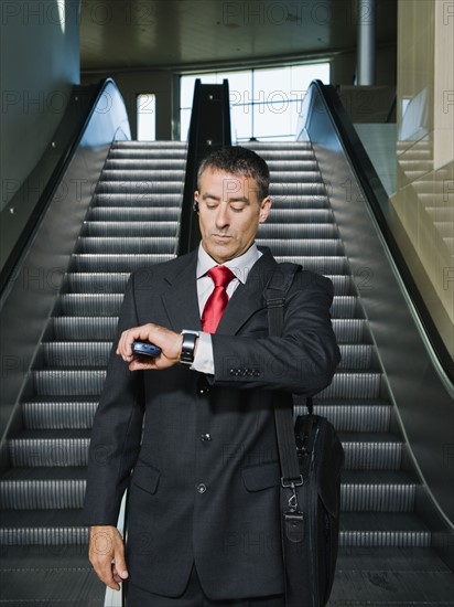 Businessman on escalator checking wristwatch. Date : 2008