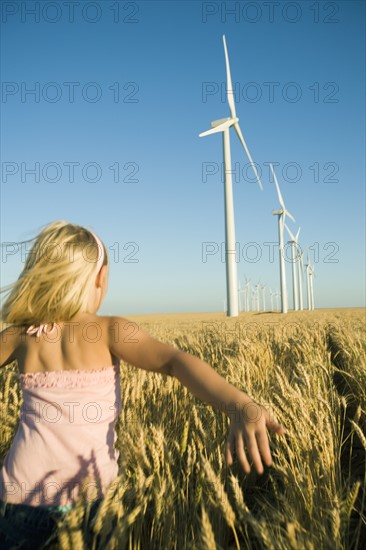 Girl running through tall wheat field on wind farm. Date : 2008