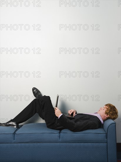 Businessman lounging on sofa with laptop. Date : 2008