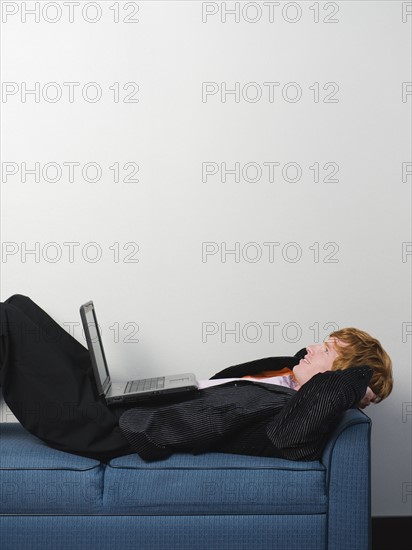 Businessman lounging on sofa with laptop. Date : 2008