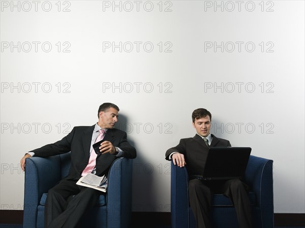 Businessmen sitting in chairs in office lobby. Date : 2008