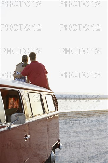 Couple watching ocean sunset from top of van. Date : 2008