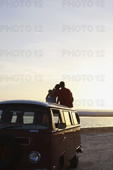 Couple watching ocean sunset from top of van. Date : 2008