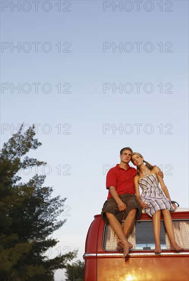 Couple watching ocean sunset from top of van. Date : 2008