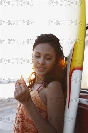 Girl leaning against surfboard on beach. Date : 2008