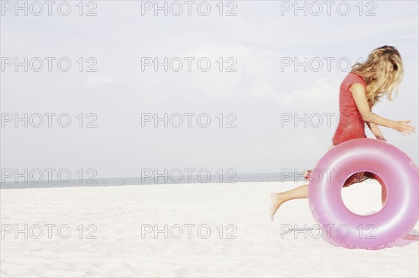 Teenage girl rolling inflatable ring on beach. Date : 2008
