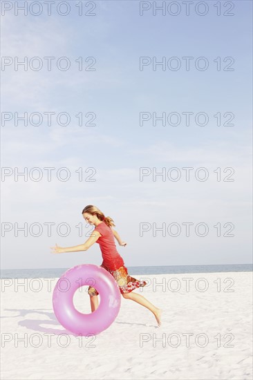 Teenage girl rolling inflatable ring on beach. Date : 2008