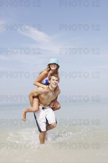 Young man carrying girlfriend on back in ocean. Date : 2008