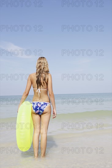 Teenage girl holding inflatable ring contemplating ocean waves. Date : 2008