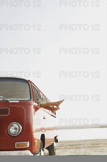 Feet sticking out of van window on beach. Date : 2008