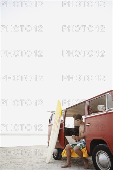 Young surfer using laptop in van on beach. Date : 2008