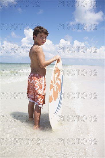 Boy holding skimboard in ocean. Date : 2008