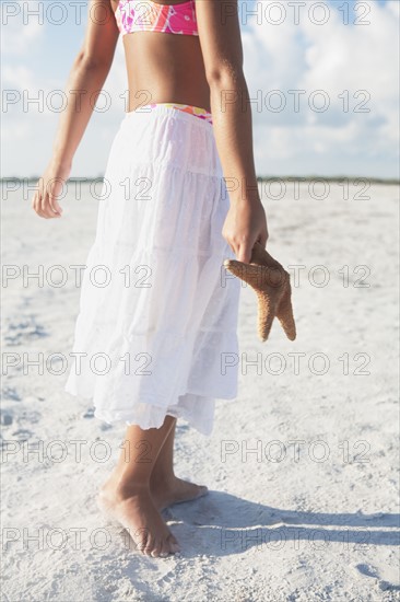 Girl walking with starfish on beach. Date : 2008