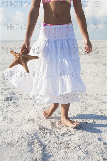 Girl walking with starfish on beach. Date : 2008