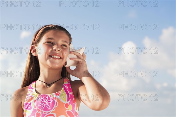 Girl holding conch shell to ear. Date : 2008