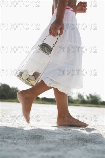 Girl on beach carrying jar of shells. Date : 2008