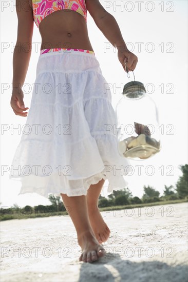 Girl on beach carrying jar of shells. Date : 2008