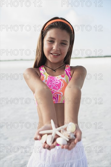 Girl on beach holding delicate starfish and shells. Date : 2008