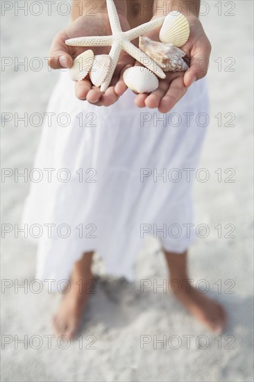 Girl on beach holding delicate starfish and shells. Date : 2008