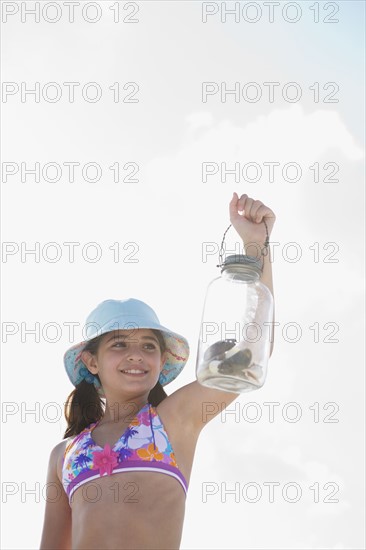 Girl at beach displaying jar of shells. Date : 2008