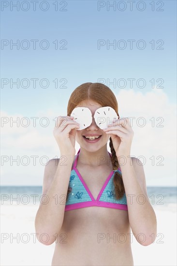 Girl on beach holding sand dollars over eyes. Date : 2008