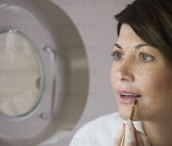 Woman applying makeup in vanity mirror.