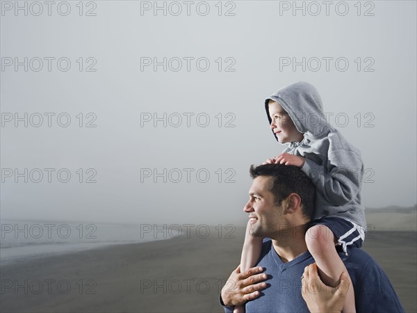 Father carrying son on shoulders on beach. Date : 2008