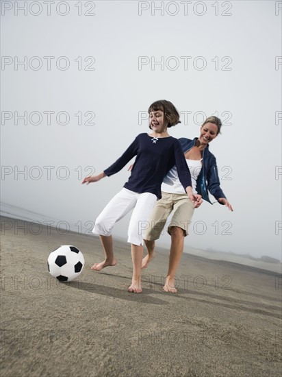 Mother and daughter kicking soccer ball on beach. Date : 2008