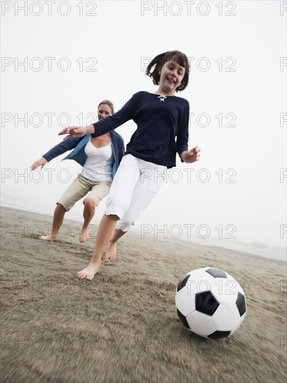 Mother and daughter playing soccer on beach. Date : 2008