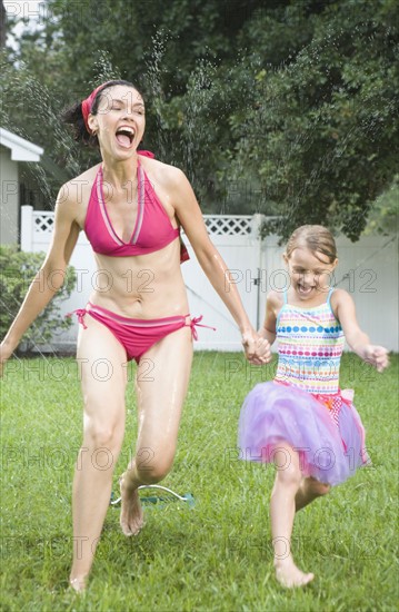 Mother and daughter running through sprinkler. Date : 2008