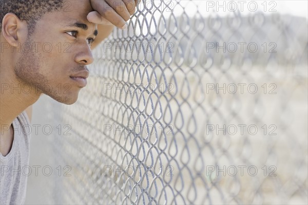 Young man leaning against chain-link fence. Date : 2008