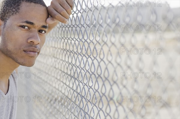 Portrait of young man leaning against chain-link fence. Date: 2008