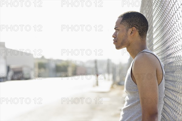 Young man leaning against chain-link fence. Date : 2008