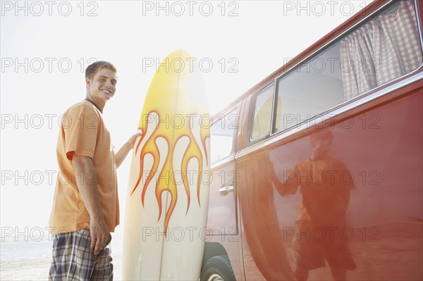 Portrait of young man holding surfboard near van. Date : 2008