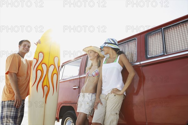 Young man with surfboard and women leaning against van. Date : 2008