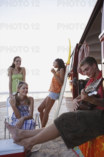 Friends lounging around van on beach. Date: 2008