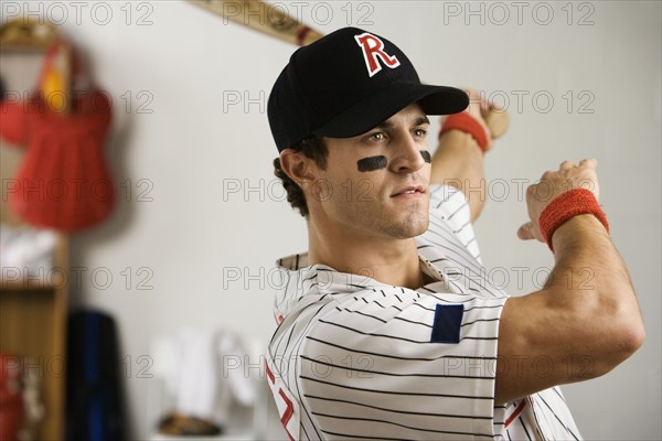 Baseball player practicing swing in locker room. Date : 2008