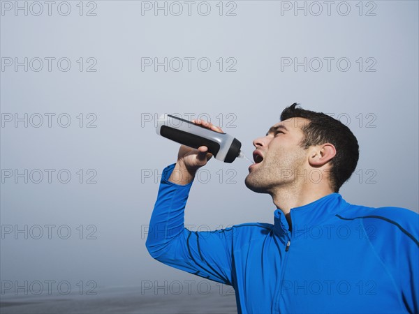 Man drinking from water bottle on foggy beach. Date : 2008