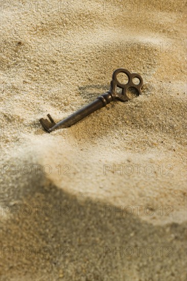 Close up of old-fashioned key in sand.