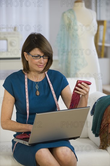 Clothing designer holding fabric and using laptop.