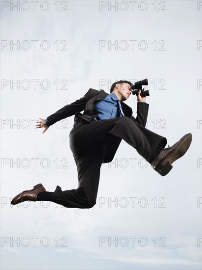 Businessman with binoculars jumping in mid-air. Date : 2008