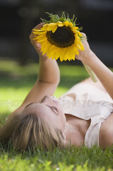 Woman laying in grass holding sunflower.