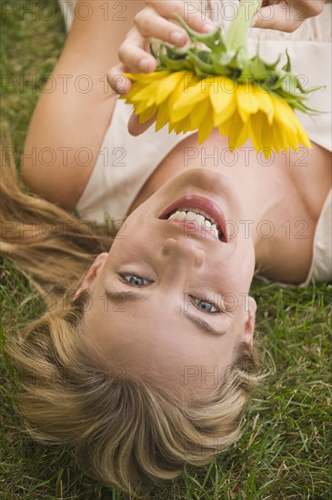 Woman laying in grass holding sunflower.