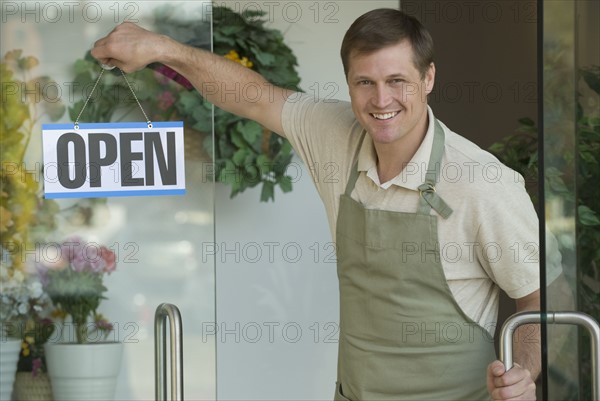 Man hanging open sign in flower shop window.
