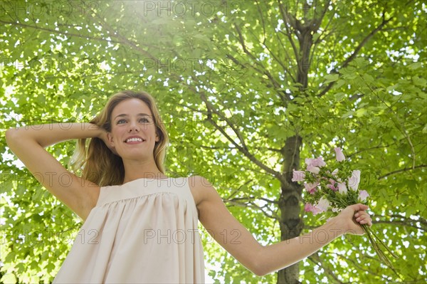 Woman with flowers standing under tree.