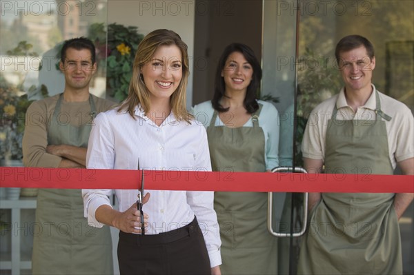 Small business owner cutting red ribbon at grand opening.