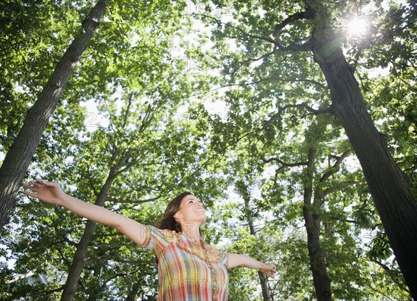 Woman standing below trees with arms outstretched. Date: 2008